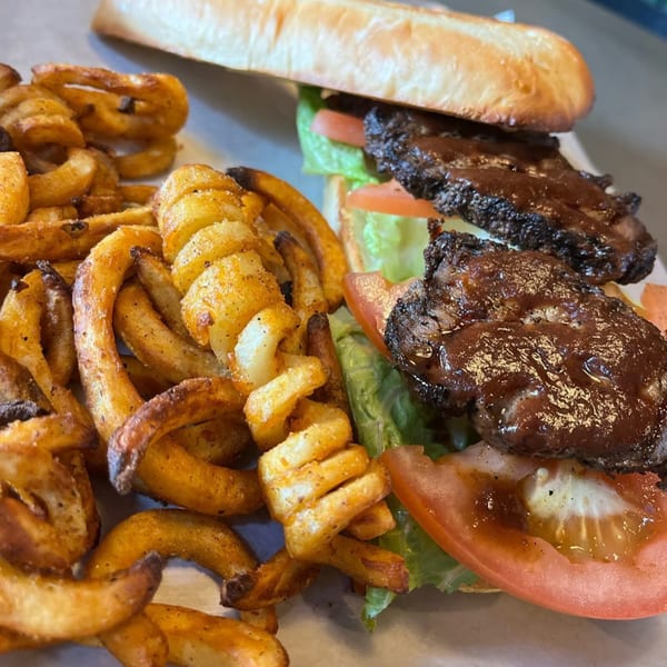 A BBQ brisket sandwich on a baguette with lettuce and tomato, served with curly fries.