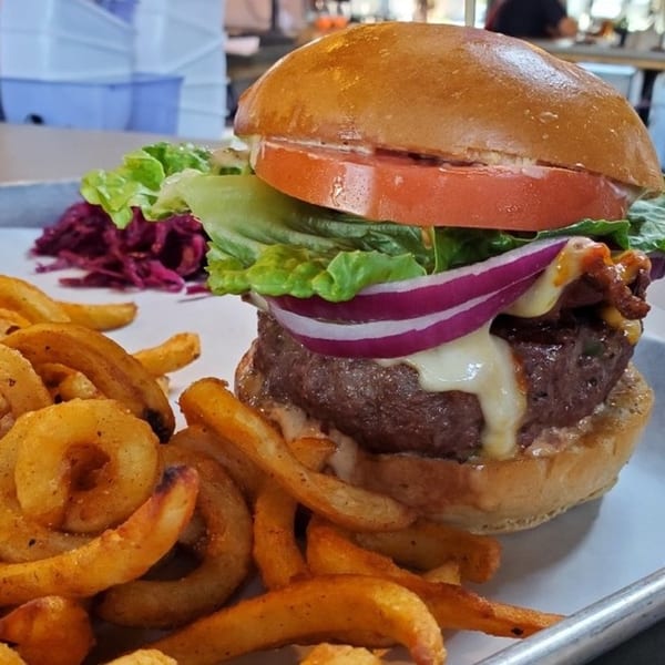 A juicy Twisted District Brew Co. burger with curly fries and red cabbage slaw.