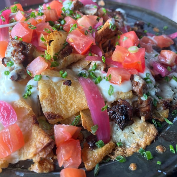 Close-up of Twisted District Brew Co.'s loaded nachos with diced tomatoes, pickled onions, and chives.