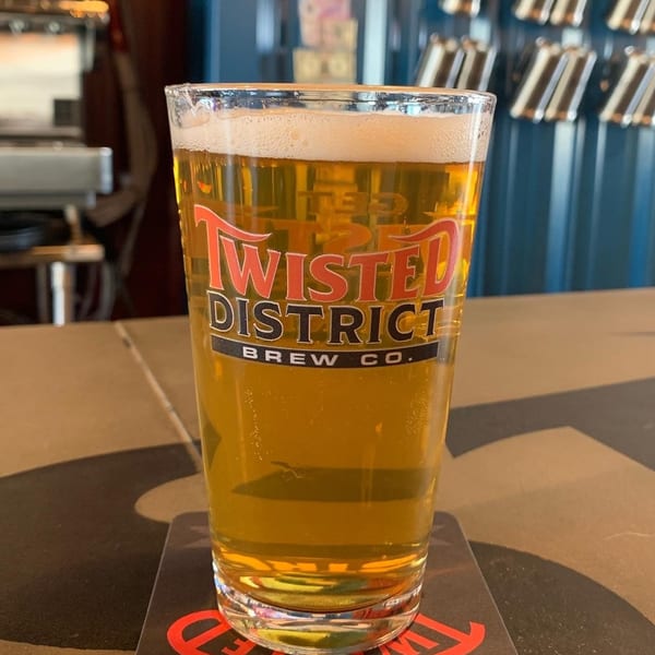 A glass of Twisted District Brew Co. beer with foam, sitting on a coaster at a bar.